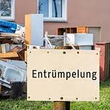 Schild mit der Aufschrift „Entrümpelung“ vor einem haufenweise abgestellten Müll.
