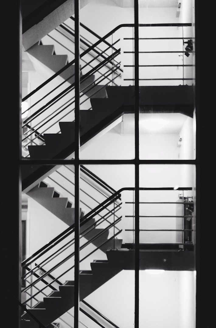Schwarz-weiß Aufnahme einer Treppe mit Geländern und rechteckigen Fenstern.